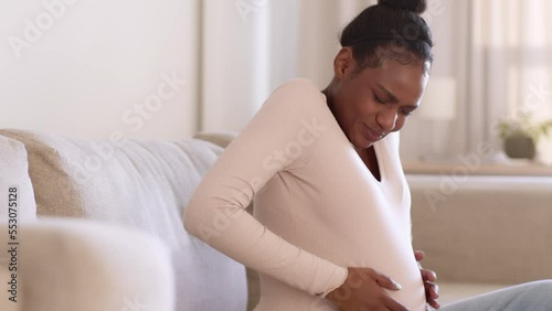 Training contractions. Young worried pregnant black woman feeling pain attack in stomach, deeply breathing at home