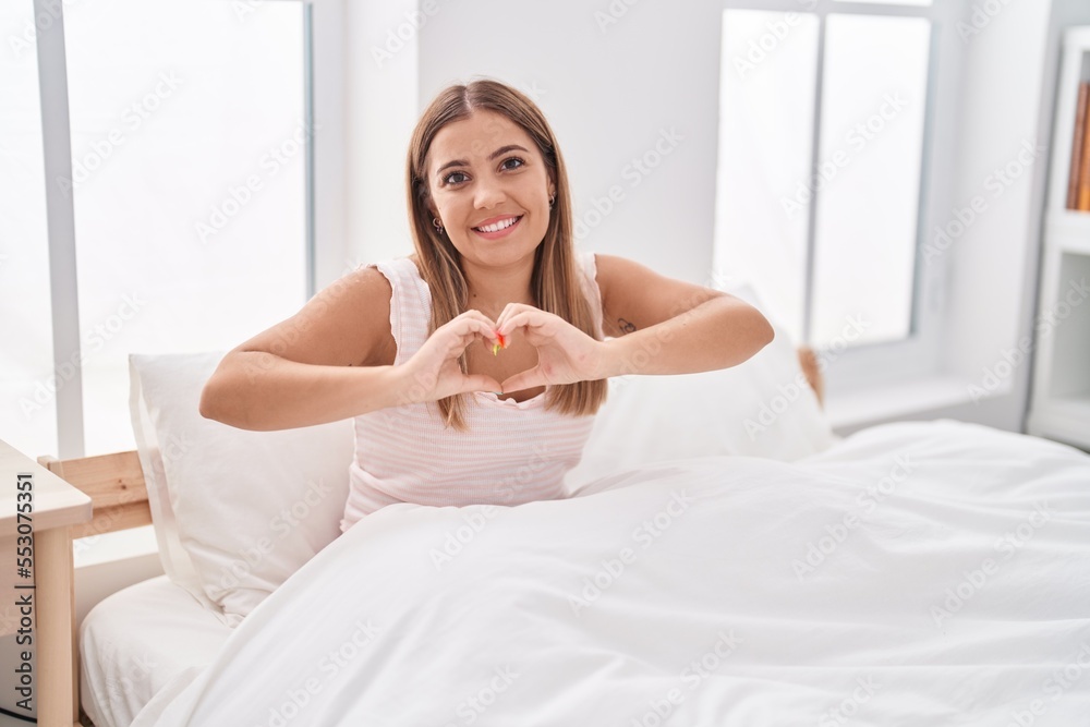 Young beautiful hispanic woman doing heart gesture sitting on bed at bedroom Young beautiful hispanic woman doing heart gesture sitting on bed at bedroom