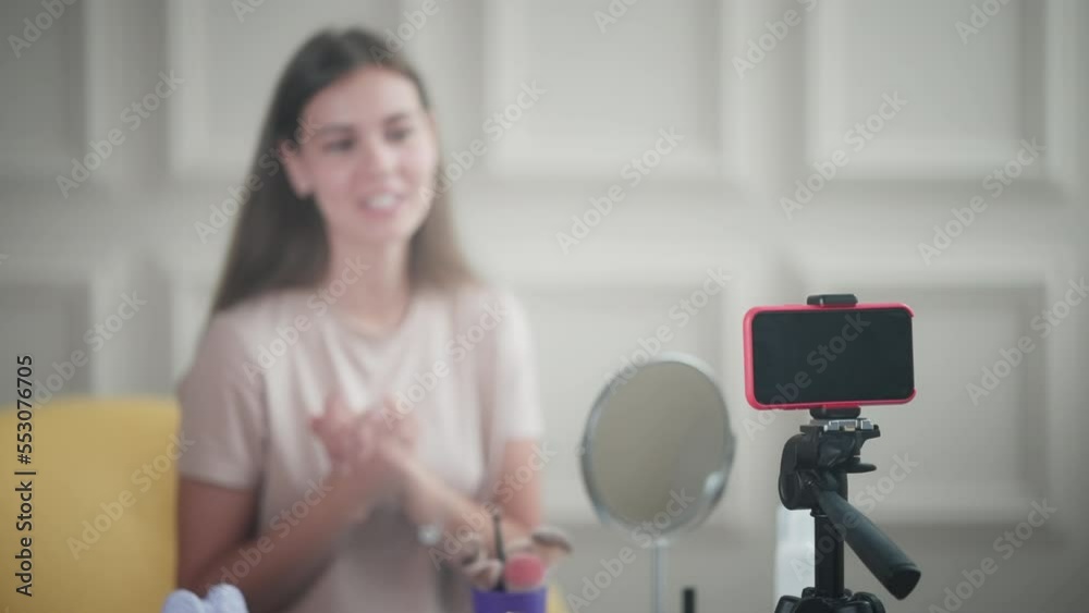 young charismatic woman is recording beauty blog, filming herself by smartphone, streaming online
