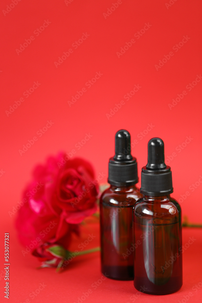 Rose essential oil. Organic oil in glass bottles set and red rose on red background.Aromatherapy and cosmetics concept.Organic natural rose oil.Organic bio cosmetics Rose essential oil. Organic oil in glass bottles set and red rose on red background.Aromatherapy and cosmetics concept.Organic natural rose oil.Organic bio cosmetics