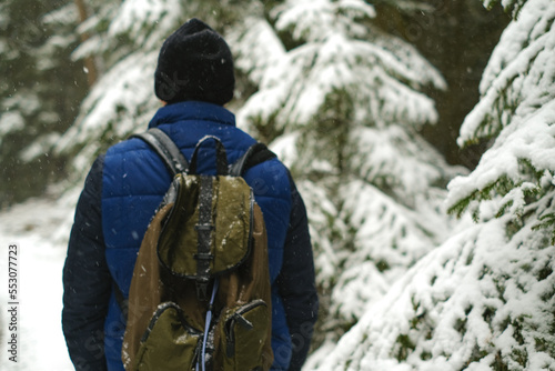  Traveler in winter snowy forest.travel and hiking in Winter season.man with a backpack in snowy weather. Snowfall in the winter forest.Man in the natural environment in the cold season © Yuliya