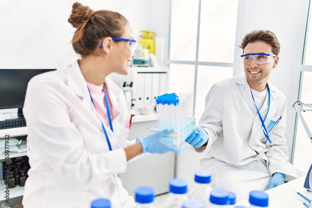 Man and woman wearing scientist uniform holding test tube at laboratory Man and woman wearing scientist uniform holding test tube at laboratory