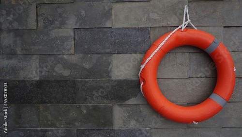 orange lifebuoy hanging in the stone wall of swimming pool. safety for people at water