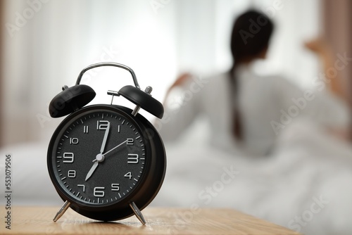 Woman stretching in bedroom, focus on alarm clock. Space for text