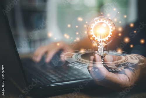 hand of a man with a light bulb And there is a gear icon in it And he is using a notebook computer. The idea of ​​inspiration from online technology. innovation idea concept.