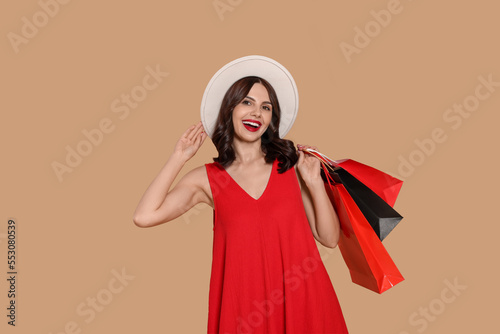 Beautiful young woman with paper shopping bags on beige background