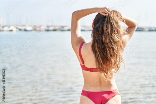 Young beautiful hispanic woman tourist wearing bikini standing on back view at beach