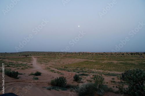 Moon set. View of Thar desert sand dunes , pre dawn light before sun rise and moon setting off in the sky. Rajasthan, India.