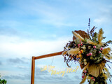 Will You Marry Me ?, LED neon light text hanging with flowers on the wooden poles on blue sky background on sunset beach.