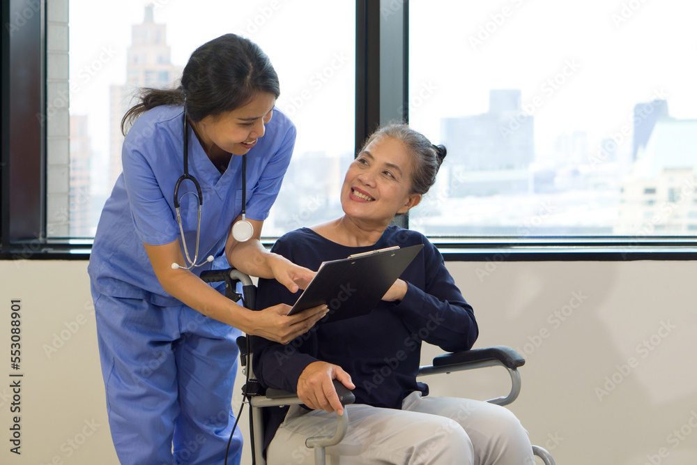 Obraz premium Woman physical therapist in blue uniform with stethoscope and clipboard explaining rehabilitation steps to an elderly in a wheelchair.