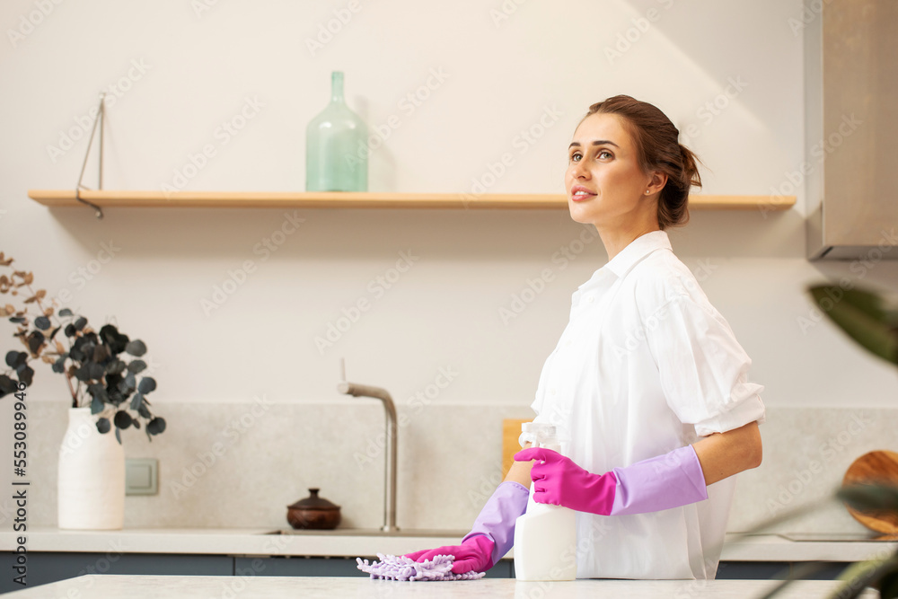 An attractive woman in rubber gloves holds a bottle of detergent in the kitchen. Cleaning products. An attractive woman in rubber gloves holds a bottle of detergent in the kitchen. Cleaning products.