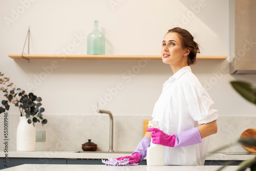 An attractive woman in rubber gloves holds a bottle of detergent in the kitchen. Cleaning products.