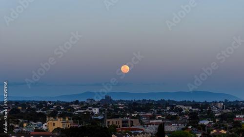 The moon is shining in a clear sky over the suburbs in Melbourne, Australia, with Mount Dandenong in the distance