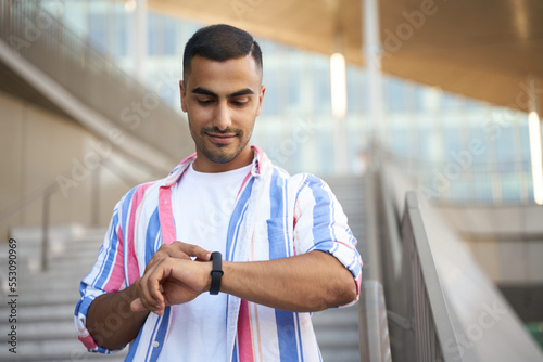 Smiling handsome middle eastern man looking at smart watch check time walking on the street   © Maria Vitkovska
