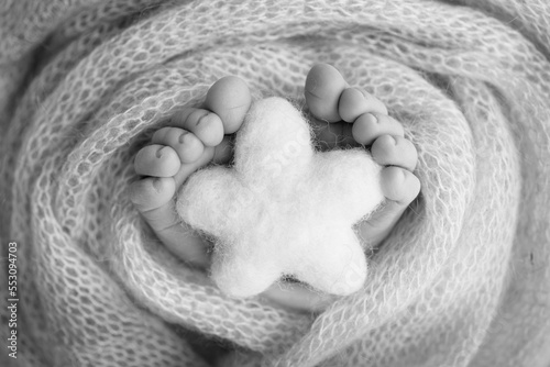 Knitted star in the legs of a baby. Soft feet of a new born in a wool blanket. Close-up of toes  heels and feet of a newborn. Macro black and white photography the tiny foot of a newborn baby. 