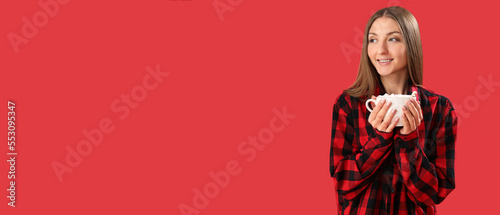 Pretty young woman in pajamas drinking hot chocolate on red background with space for text