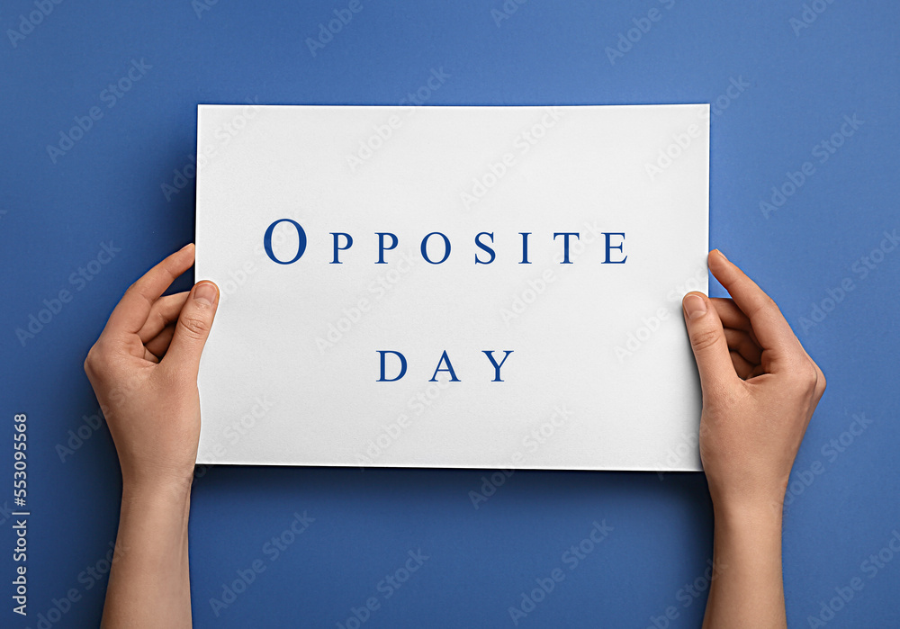 Female hands holding paper sheet with text OPPOSITE DAY on blue background Female hands holding paper sheet with text OPPOSITE DAY on blue background
