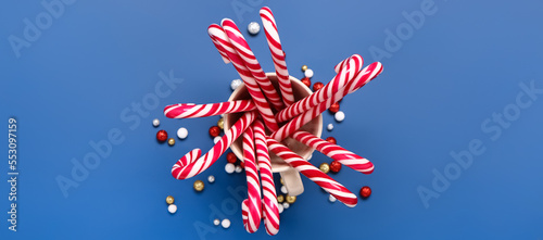 Cup with tasty candy canes on blue background, top view