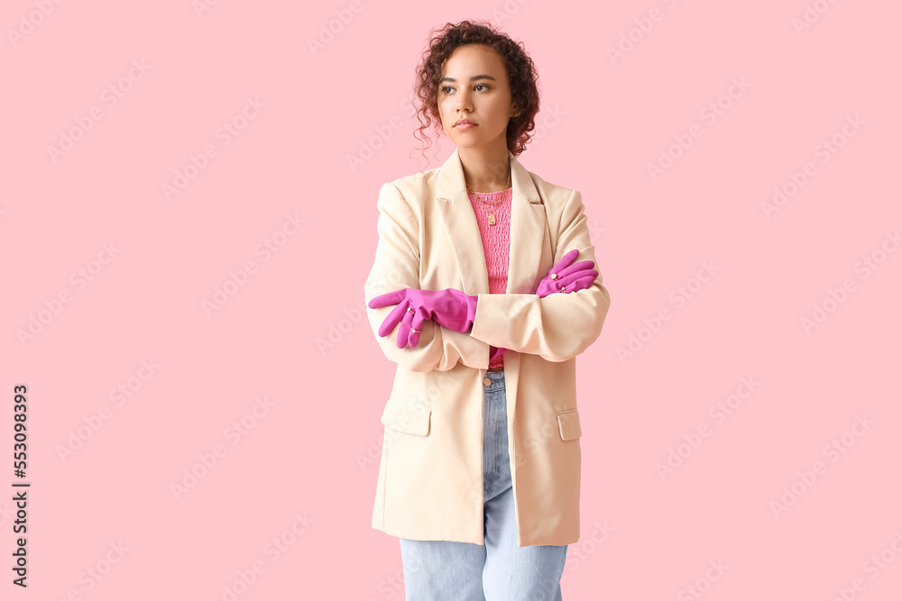 Young African-American woman in rubber gloves and jewelry standing with crossed hands on color background Young African-American woman in rubber gloves and jewelry standing with crossed hands on color background