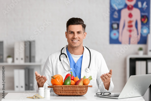 Male doctor with vitamins and vegetables sitting at table in clinic