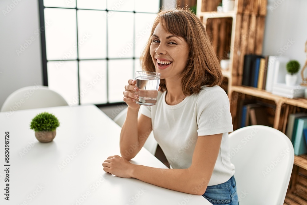 Young caucasian woman drinking water sitting on table at home Young caucasian woman drinking water sitting on table at home