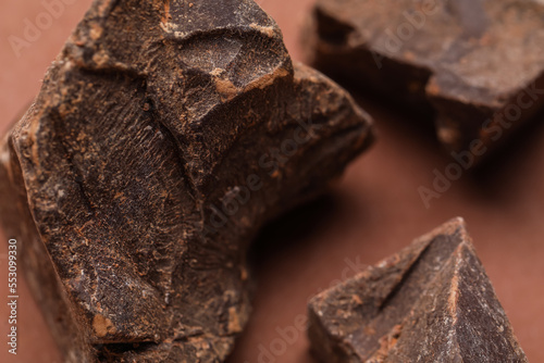 Pieces of delicious chocolate on brown background, closeup