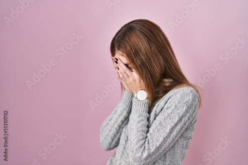 Beautiful woman standing over pink background with sad expression covering face with hands while crying. depression concept. © Krakenimages.com