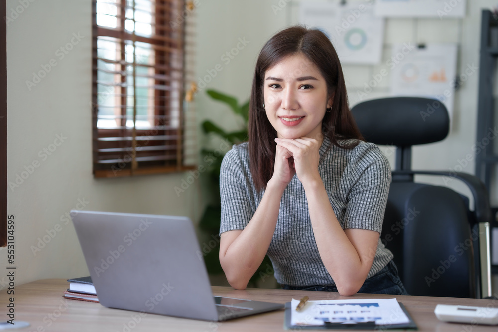 Attractive Asian businesswoman enjoying working using laptop at office. Looking at camera. Attractive Asian businesswoman enjoying working using laptop at office. Looking at camera.