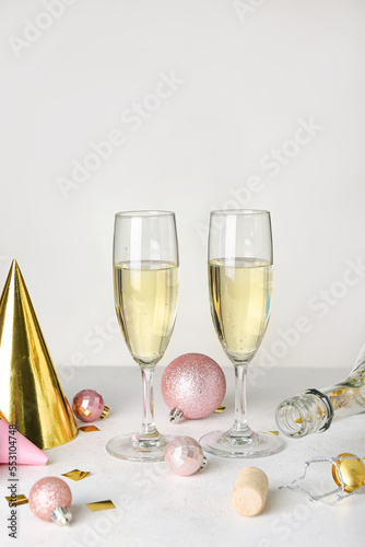 Glasses of champagne, bottle, Christmas balls and party hats on light background