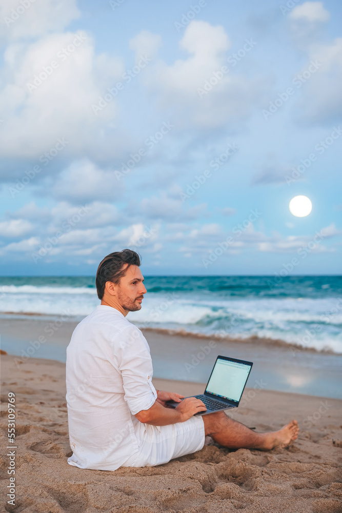 Man with laptop on the beach at sunset 