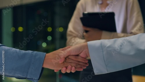 Closeup multiracial group of young creative people in smart casual wear discussing business shaking hand together while standing in modern night office. Partner cooperation, coworker teamwork concept. photo