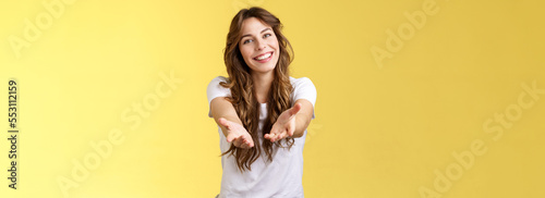 Come closer take my hand. Cheerful lovely charismatic tender woman extend arms forward camera wanna hold receive charming gift tilt head smiling pleased grateful stand yellow background photo