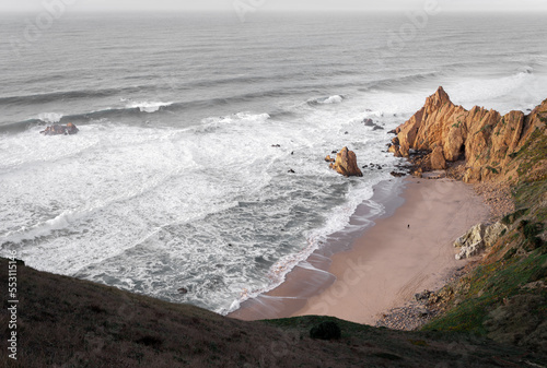 A wide view of adraga beach coast and a hill covered with vegetation in Sintra, Portugal photo