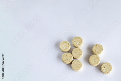 Supplements with chewable tablets DGL liquorice root. Copy space. Round puck tablets of beige color with dark droplets on a white background view from above.