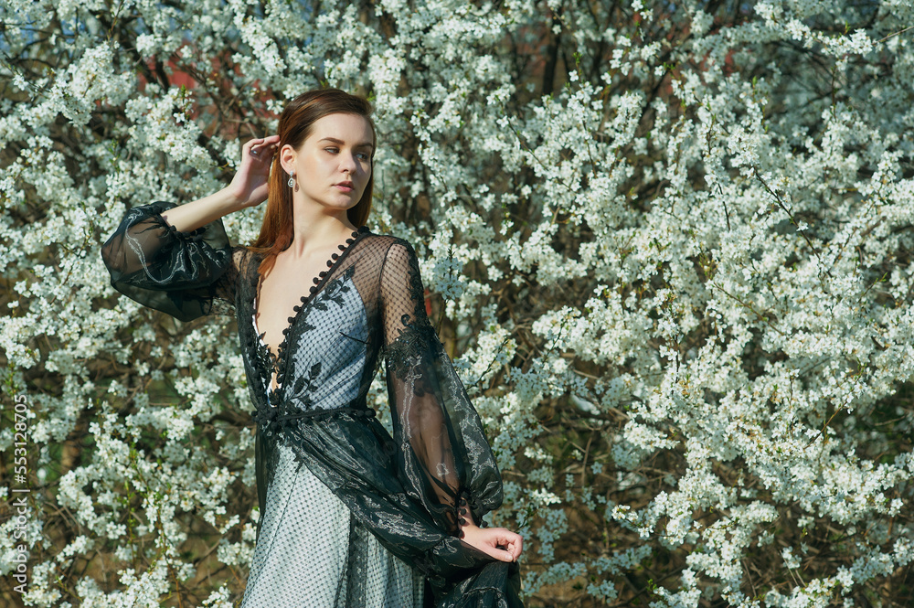 Portrait of a young beautiful girl in a spring blooming garden. Woman in an evening designer dress