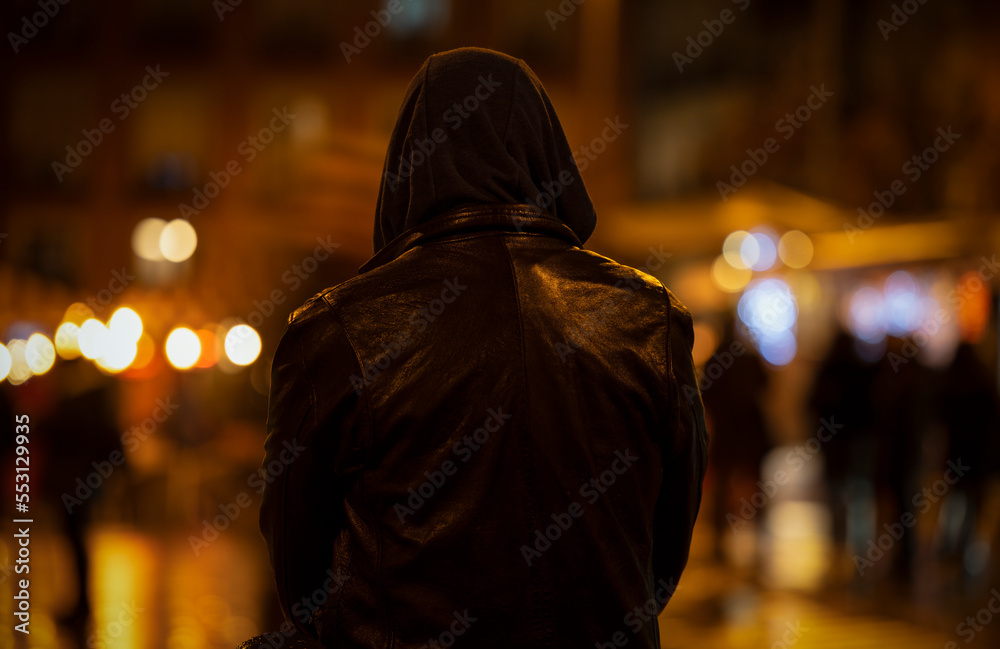 Rear view of adult man with hood on street at night Rear view of adult man with hood on street at night