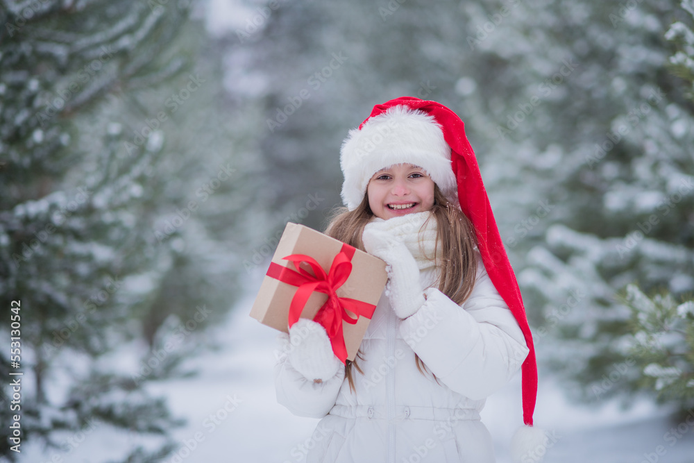 portrait of a happy girl in a Santa hat with a gift box in her hands in nature in a winter park, happy Christmas