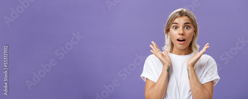 Close-up shot of charmed and impressed good-looking caucasian girlfriend with blond hair and tattoos on arms raising hands in amazed and excited gesture opening mouth and gazing mesmerized at camera