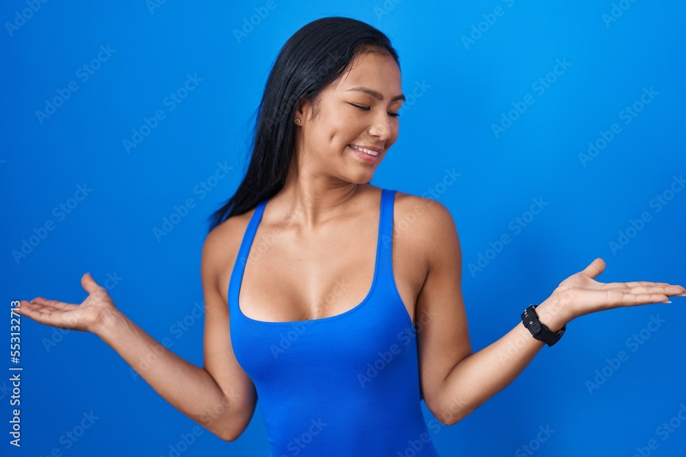 Hispanic woman standing over blue background smiling showing both hands open palms, presenting and advertising comparison and balance Hispanic woman standing over blue background smiling showing both hands open palms, presenting and advertising comparison and balance