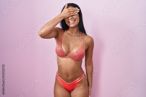 Hispanic woman wearing bikini smiling and laughing with hand on face covering eyes for surprise. blind concept. © Krakenimages.com