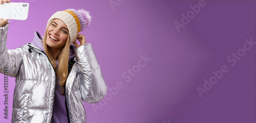 Joyful carefree charming blond girl having fun wanna post pictures from ski resort vacation taking seflie holding smartphone mimicking show tongue winking look mobile display, purple background photo