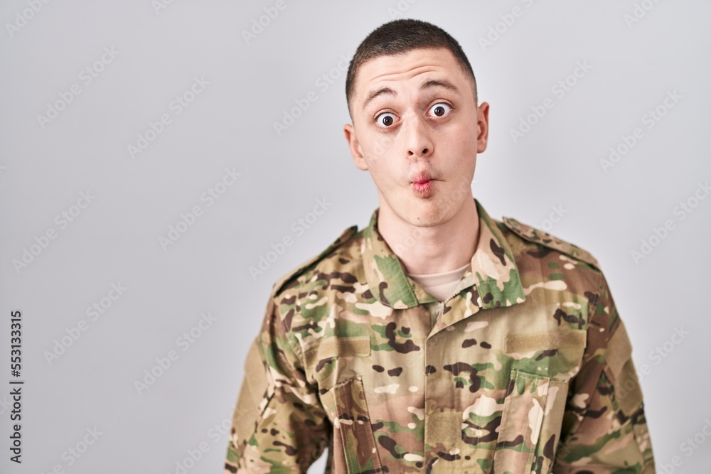Young man wearing camouflage army uniform making fish face with lips, crazy and comical gesture. funny expression.
