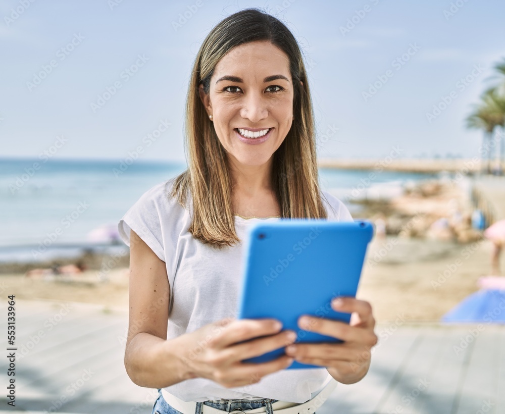 Young hispanic woman smiling confident using touchpad at seaside