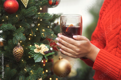 Woman in a red sweater warms her hands and holding a glass of hot wine at the Christmas market in the city