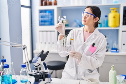 Young woman wearing scientist uniform holding test tubes with flowers at laboratory