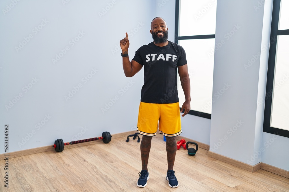 African american man working at fitness gym smiling with an idea or question pointing finger up with happy face, number one