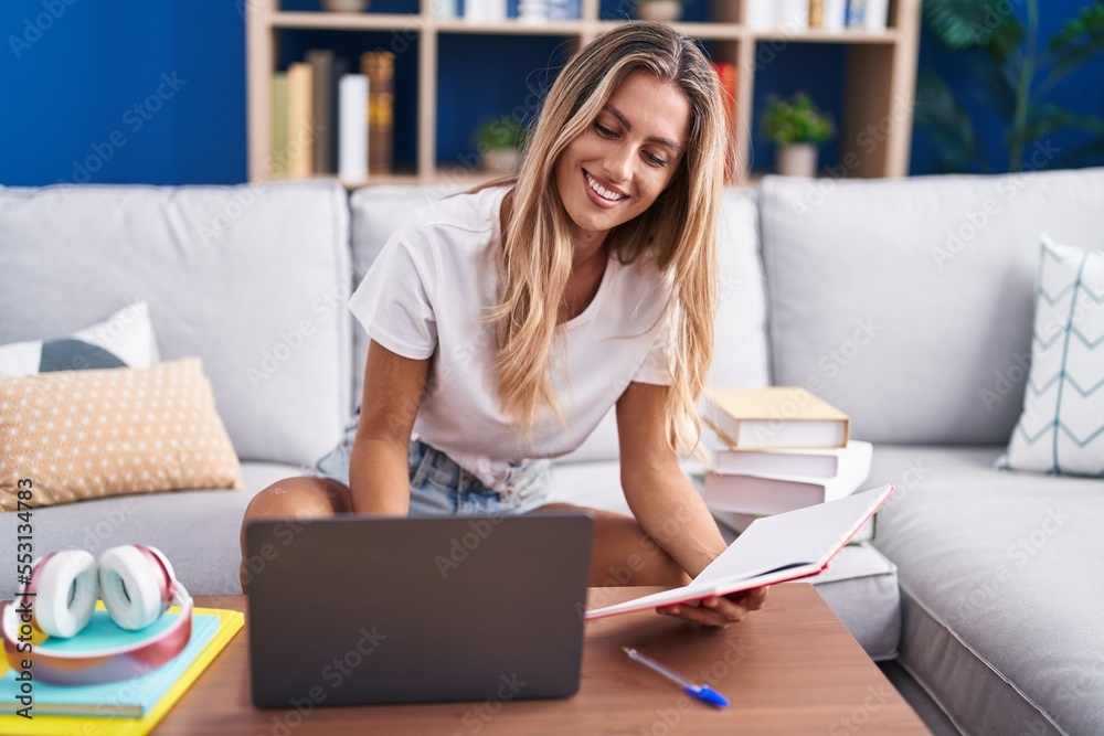 Young blonde woman student sitting on sofa reading notebook at home
