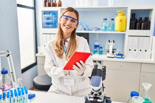 Young blonde woman wearing scientist uniform using laptop at laboratory