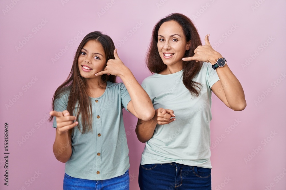 Young mother and daughter standing over pink background smiling doing talking on the telephone gesture and pointing to you. call me. Young mother and daughter standing over pink background smiling doing talking on the telephone gesture and pointing to you. call me.