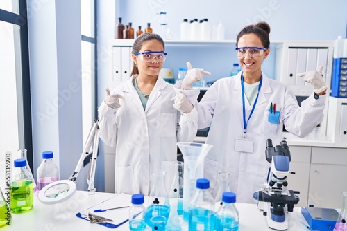 Young mother and daughter at scientist laboratory looking confident with smile on face, pointing oneself with fingers proud and happy.